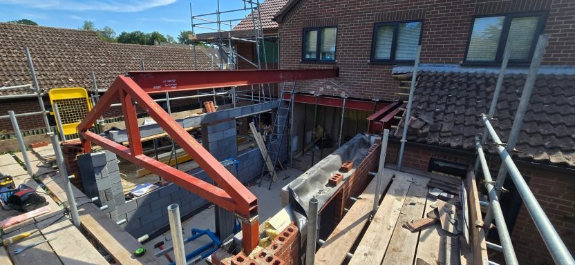 Red primed steel frame installed on a house extension with scaffolding, Norfolk