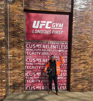 Person standing in front of the UFC Gym London entrance, wearing an orange jacket.