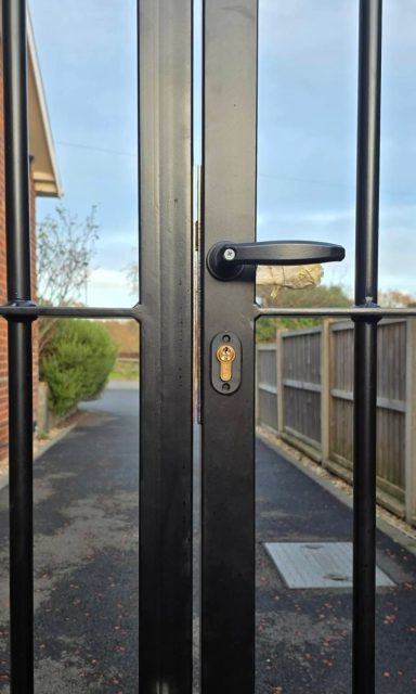 Black metal gate with a handle, leading to a path and greenery beyond.