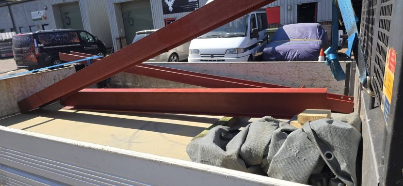 Red primed steel beams strapped together ready for delivery, Norwich Red oxide primed steel I-beams loaded on a flatbed trailer outside industrial units